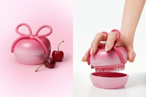 The pink Ribbon Cherry Glass Hairbrush with its bow-shaped cover, beside cherries